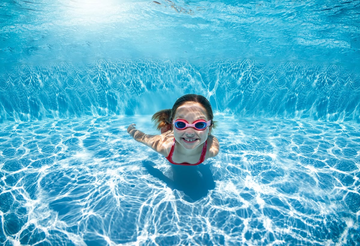 Portrait of a happy girl with goggles swimming under water in swimming pool as a summer concept