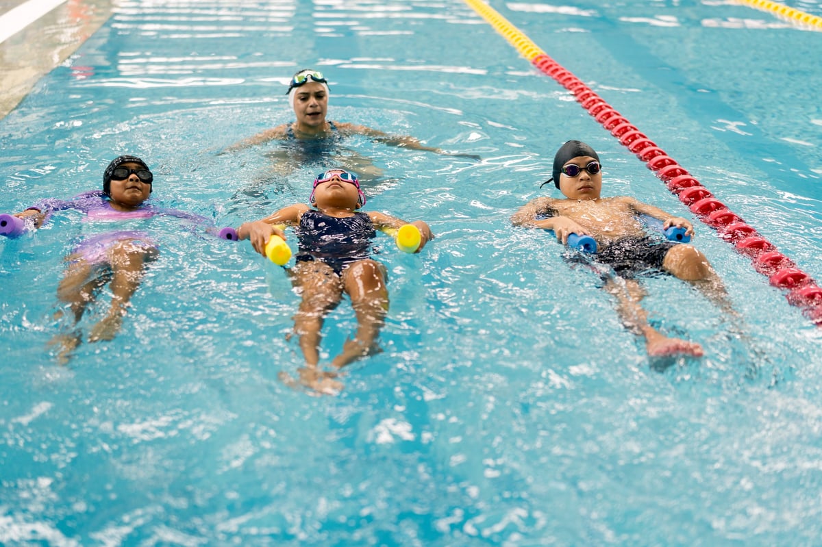 Children practicing backstroke and floating with swimming aids in a pool with their instructor during a swim lesson