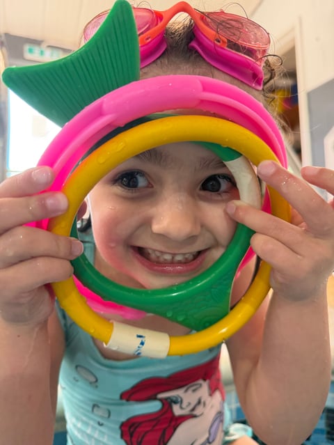 Young child smiling while holding colorful stacking rings around their face